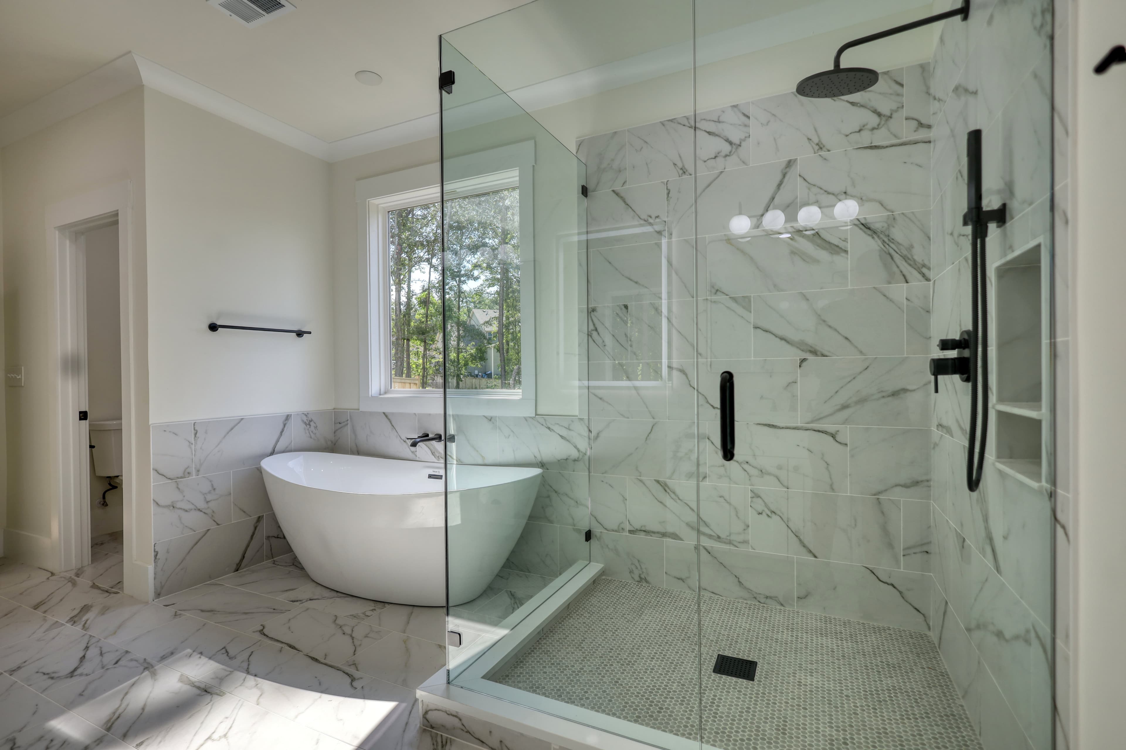 Modern bathroom featuring a white freestanding bathtub and a glass-enclosed marble tile walk-in shower.