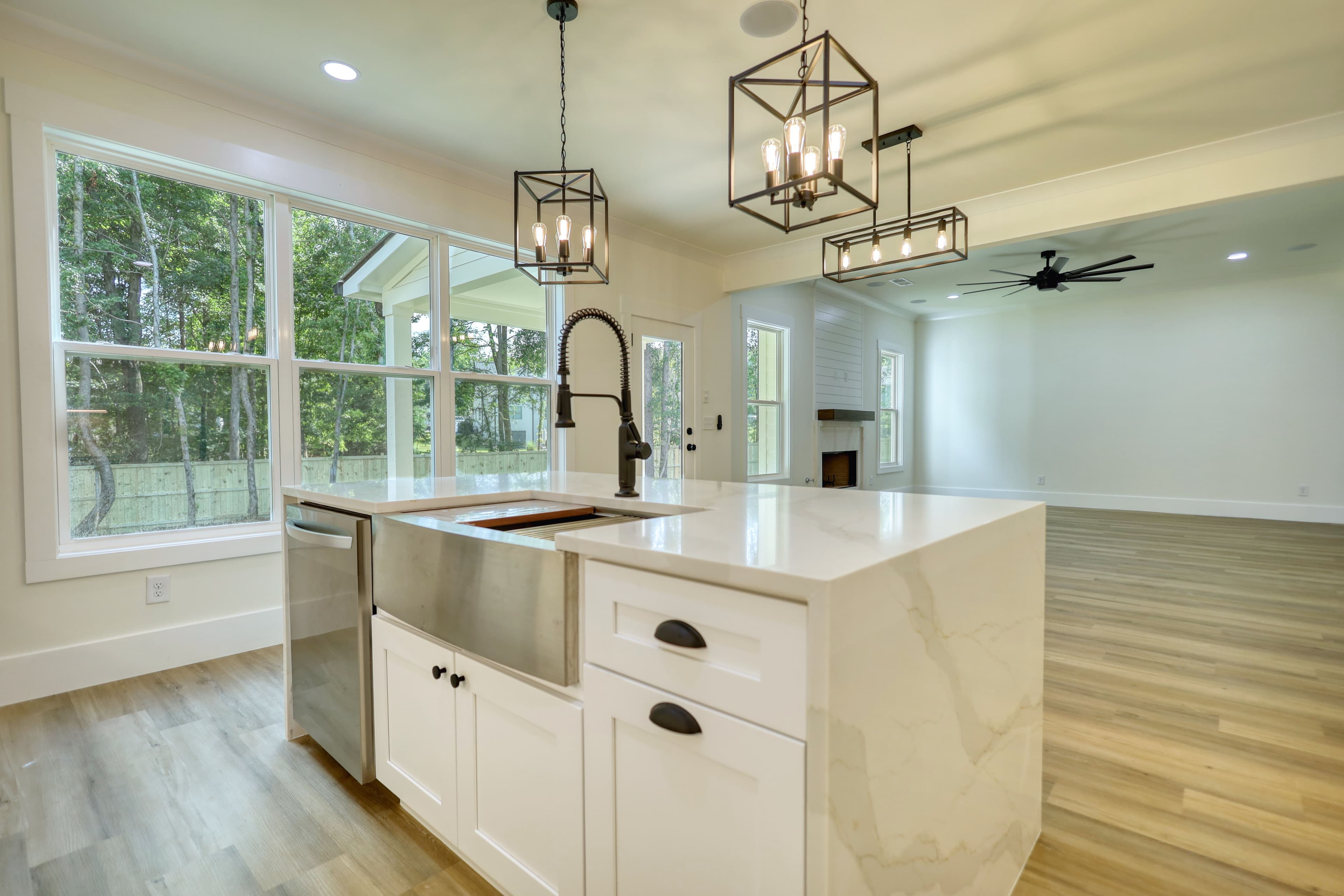 Modern kitchen with white marble island, stainless farmhouse sink, and black geometric pendant lights.
